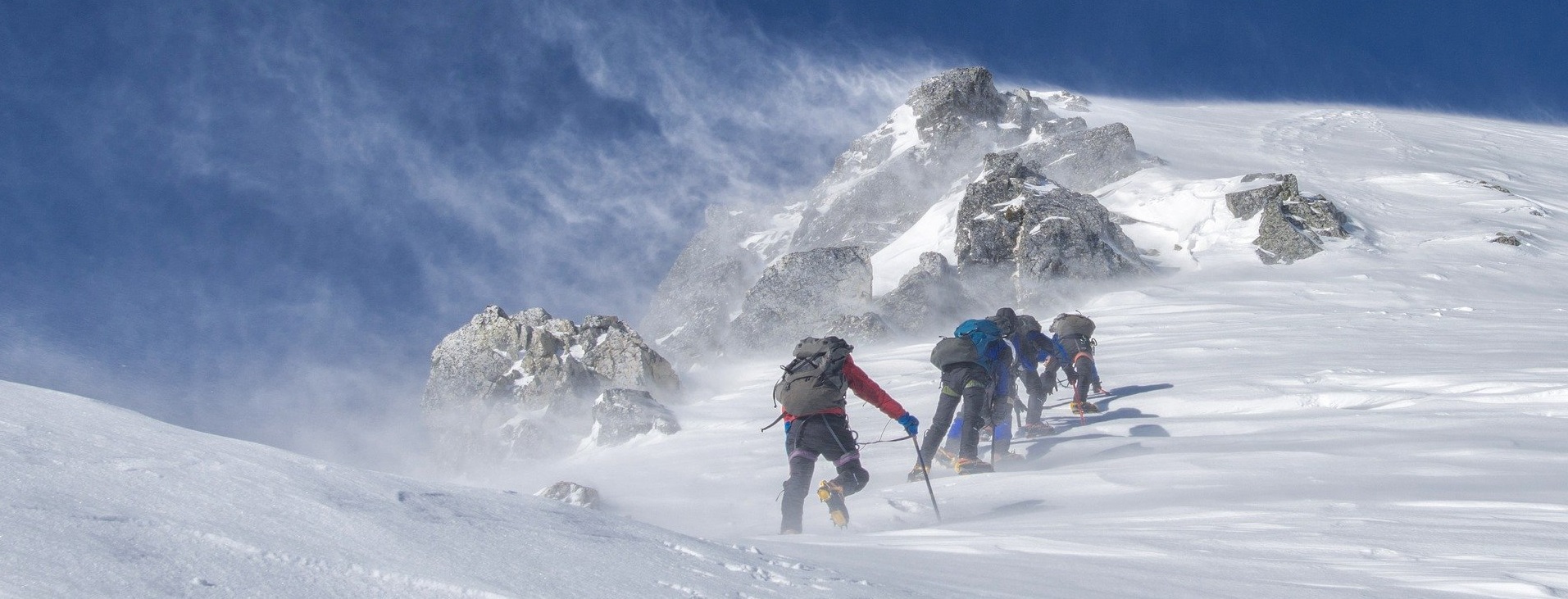 Eine Gruppe Bergsteiger erklimmt einen verschneiten Gipfel bei blauem Himmel